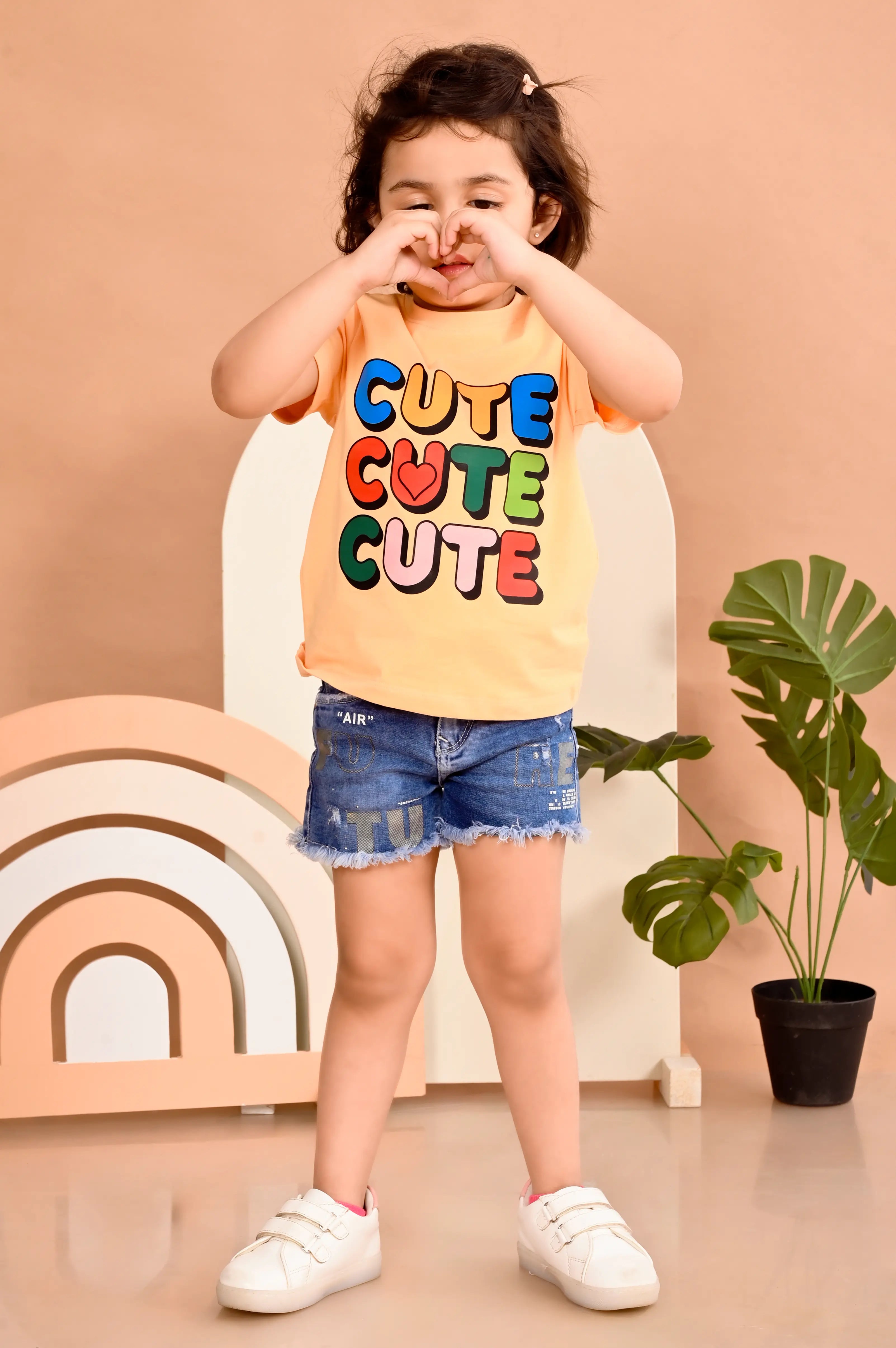 Child wearing a 'CUTE CUTE CUTE' shirt with colorful letters on a beige background