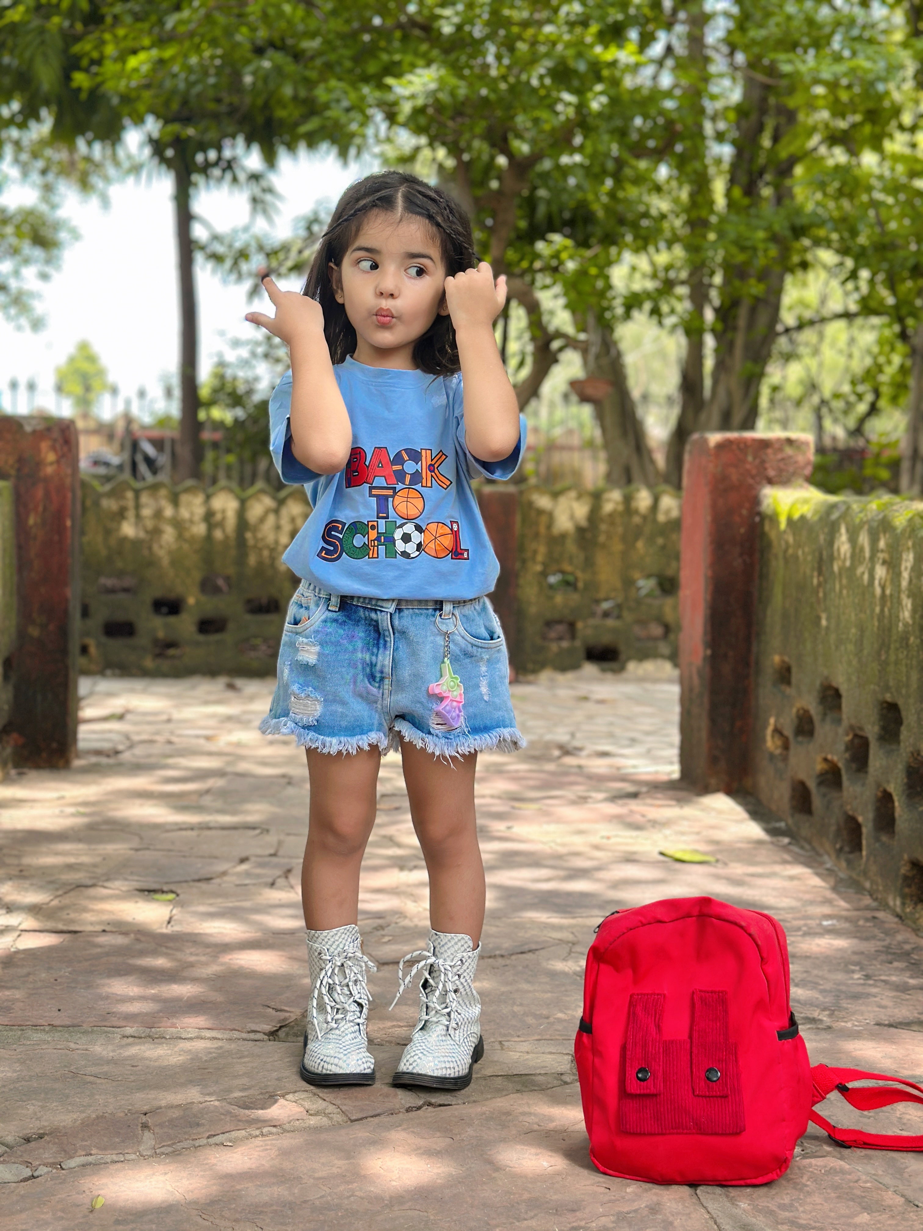 Child wearing a 'Back to School' shirt with a red backpack outdoors.