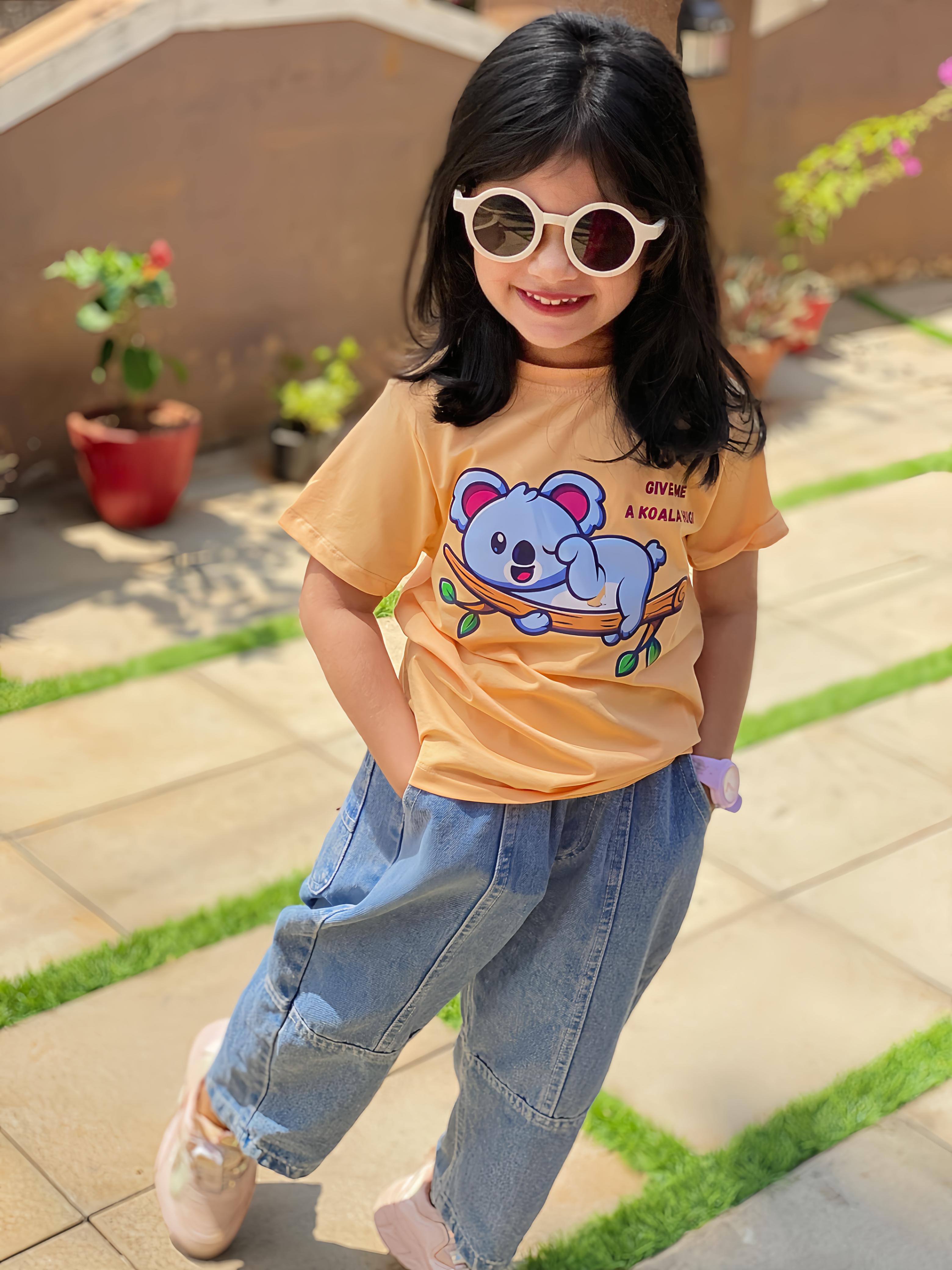 Child wearing a yellow t-shirt with a cartoon design and blue jeans outdoors.