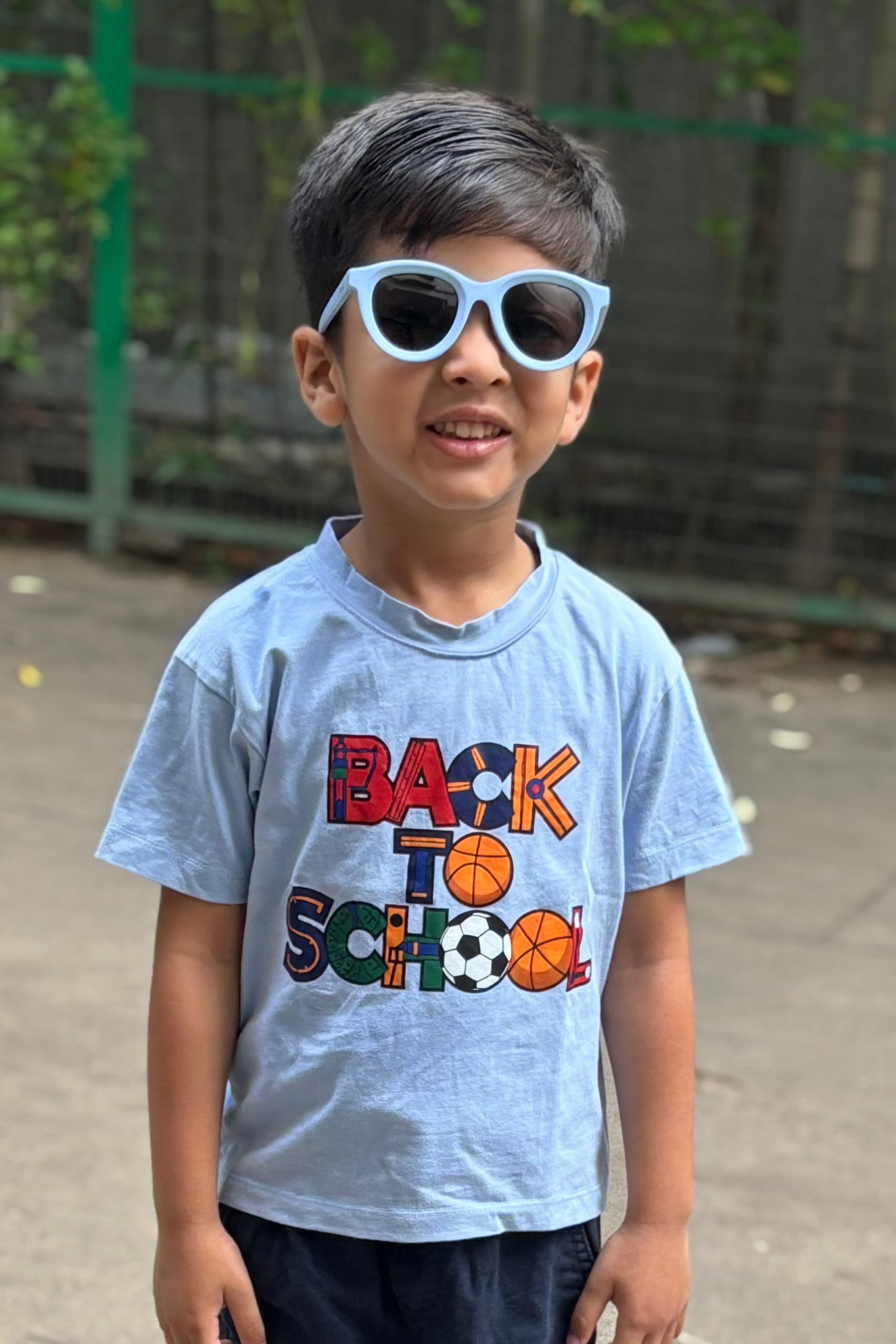 Child wearing a 'Back to School' t-shirt with sunglasses outdoors.