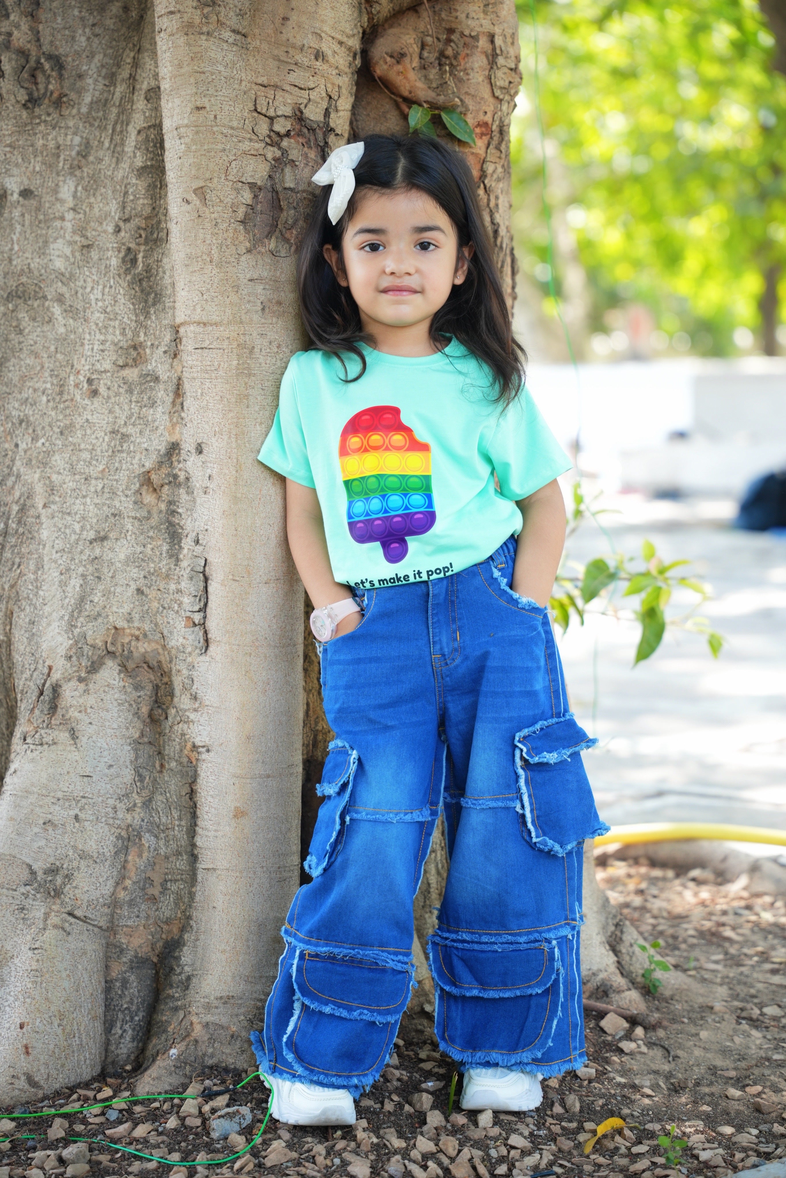 Child wearing a colorful shirt and blue jeans standing next to a tree